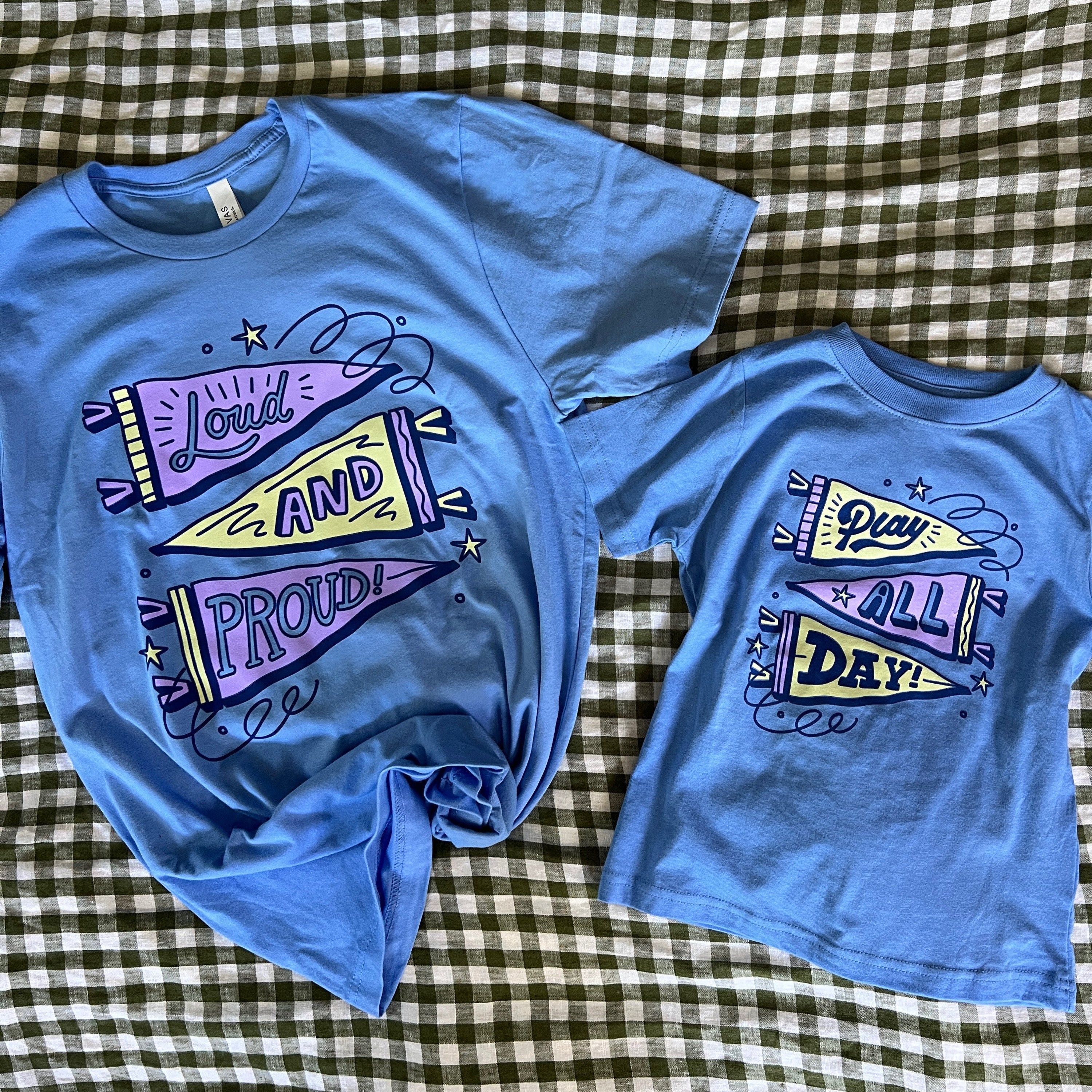 Two blue t-shirts with colorful graphics on a checkered fabric background